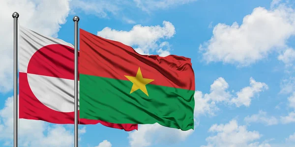 Bandera de Groenlandia y Burkina Faso ondeando en el viento contra el cielo azul nublado blanco juntos. Concepto diplomático, relaciones internacionales . — Foto de Stock