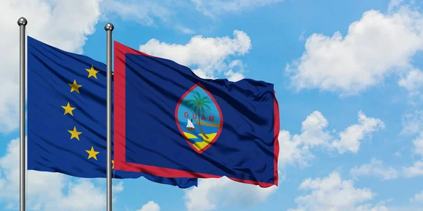 Bandera de la Unión Europea y Guam ondeando en el viento contra el cielo azul nublado blanco juntos. Concepto diplomático, relaciones internacionales . — Foto de Stock