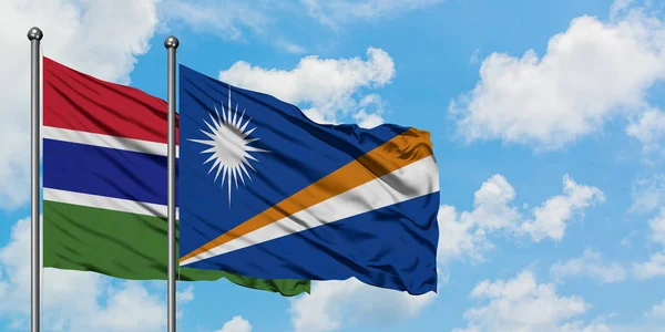 Gambia und die Marshallinseln wehen gemeinsam im Wind vor dem wolkenverhangenen blauen Himmel. Diplomatie-Konzept, internationale Beziehungen. — Stockfoto