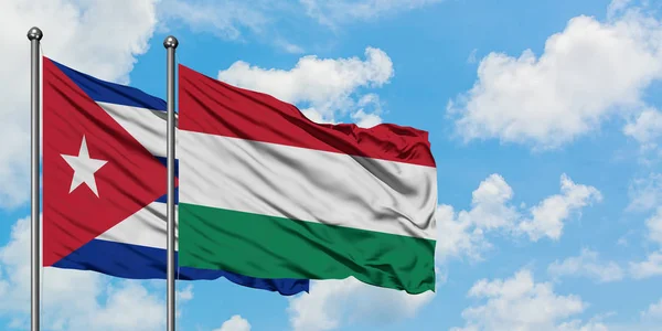 Kubas und Ungarns Flagge wehen gemeinsam im Wind vor dem weiß-wolkenverhangenen blauen Himmel. Diplomatie-Konzept, internationale Beziehungen. — Stockfoto