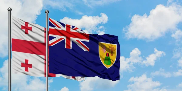 Bandera de Georgia y las Islas Turcas y Caicos ondeando en el viento contra el cielo azul nublado blanco juntos. Concepto diplomático, relaciones internacionales . — Foto de Stock