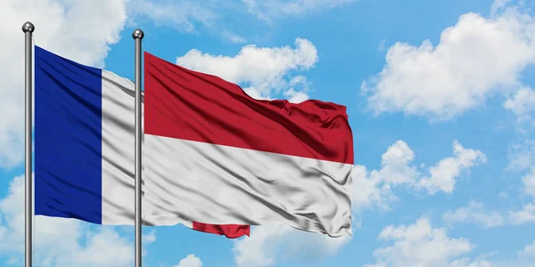 Francja i Indonezja flaga machając w wiatr przed białym zachmurzone błękitne niebo razem. Koncepcja dyplomacji, stosunki międzynarodowe. — Zdjęcie stockowe