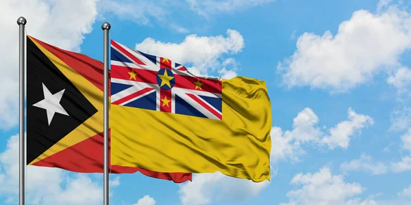 Timor Oriental y la bandera de Niue ondeando en el viento contra el cielo azul nublado blanco juntos. Concepto diplomático, relaciones internacionales . — Foto de Stock