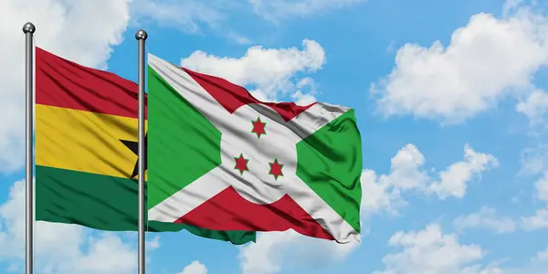 Bandera de Ghana y Burundi ondeando en el viento contra el cielo azul nublado blanco juntos. Concepto diplomático, relaciones internacionales . — Foto de Stock