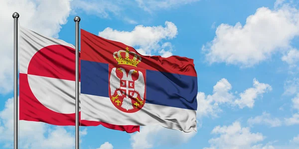 Bandera de Groenlandia y Serbia ondeando en el viento contra el cielo azul nublado blanco juntos. Concepto diplomático, relaciones internacionales . — Foto de Stock