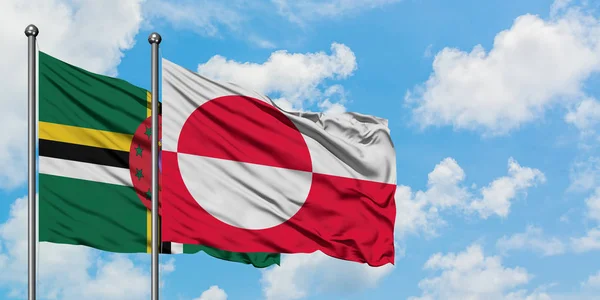 Dominica y la bandera de Groenlandia ondeando en el viento contra el cielo azul nublado blanco juntos. Concepto diplomático, relaciones internacionales . — Foto de Stock