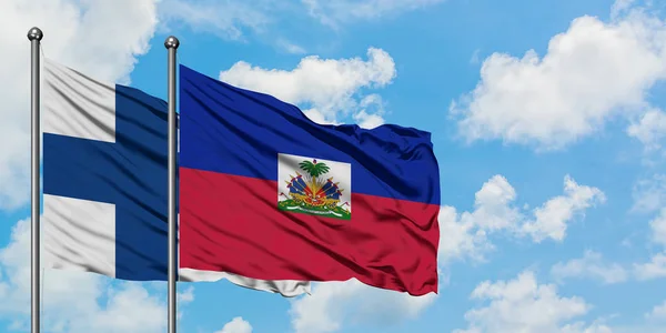 Finland en Haïti vlag zwaaien in de wind tegen witte bewolkte blauwe hemel samen. Diplomatie concept, internationale betrekkingen. — Stockfoto