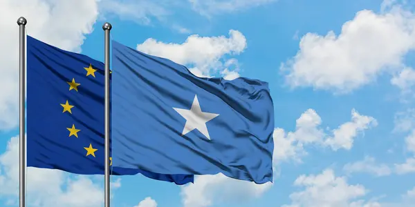 Bandera de la Unión Europea y Somalia ondeando en el viento contra el cielo azul nublado blanco juntos. Concepto diplomático, relaciones internacionales . — Foto de Stock