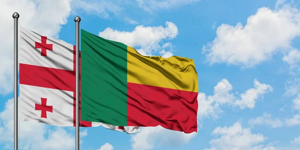 Bandera de Georgia y Benín ondeando en el viento contra el cielo azul nublado blanco juntos. Concepto diplomático, relaciones internacionales . — Foto de Stock