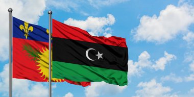 Guadeloupe ve Libya bayrağı birlikte beyaz bulutlu mavi gökyüzüne karşı rüzgarda sallayarak. Diplomasi kavramı, uluslararası ilişkiler.