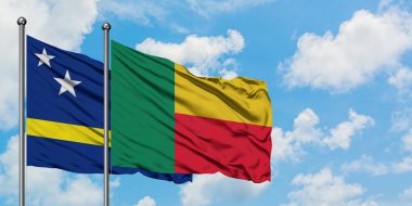 Curacao ve Benin bayrağı birlikte beyaz bulutlu mavi gökyüzüne karşı rüzgarda sallayarak. Diplomasi kavramı, uluslararası ilişkiler.