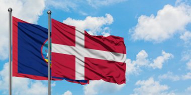 Guam ve Danimarka bayrağı birlikte beyaz bulutlu mavi gökyüzüne karşı rüzgarda sallayarak. Diplomasi kavramı, uluslararası ilişkiler.