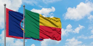 Guam ve Benin bayrağı birlikte beyaz bulutlu mavi gökyüzüne karşı rüzgarda sallayarak. Diplomasi kavramı, uluslararası ilişkiler.