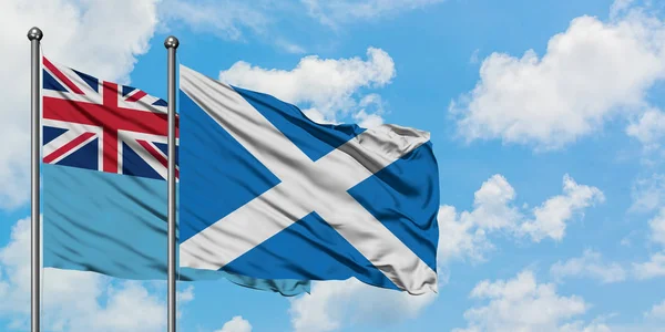 Bandera de Fiji y Escocia ondeando en el viento contra el cielo azul nublado blanco juntos. Concepto diplomático, relaciones internacionales . — Foto de Stock