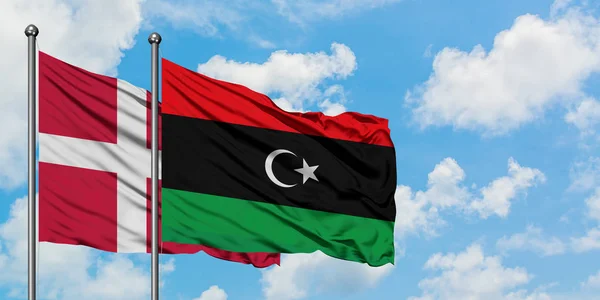 Bandera de Dinamarca y Libia ondeando en el viento contra el cielo azul nublado blanco juntos. Concepto diplomático, relaciones internacionales . — Foto de Stock