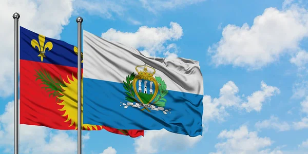 Guadalupe y la bandera de San Marino ondeando en el viento contra el cielo azul nublado blanco juntos. Concepto diplomático, relaciones internacionales . — Foto de Stock