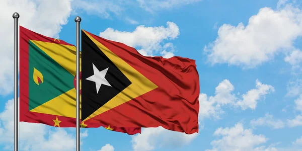 Bandera de Granada y Timor Oriental ondeando en el viento contra el cielo azul nublado blanco juntos. Concepto diplomático, relaciones internacionales . — Foto de Stock