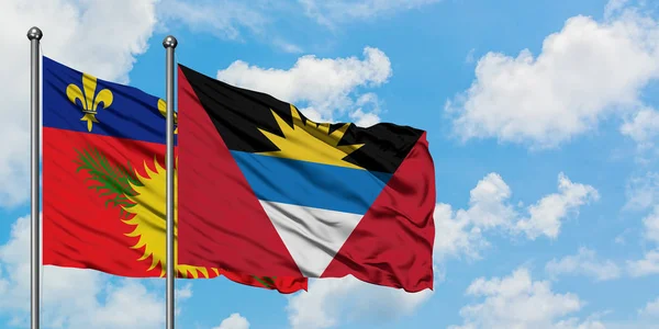 Guadeloupe ve Antigua ve Barbuda bayrağı birlikte beyaz bulutlu mavi gökyüzüne karşı rüzgarda sallayarak. Diplomasi kavramı, uluslararası ilişkiler. — Stok fotoğraf
