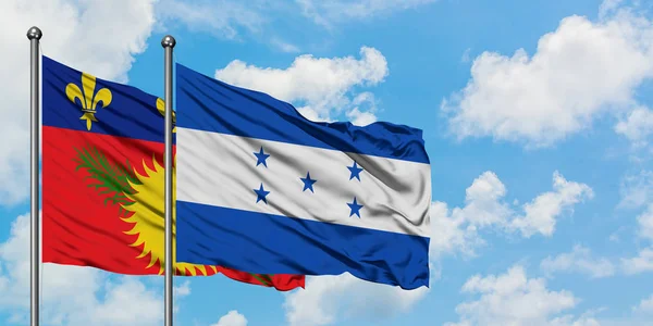 Guadalupe y la bandera de Honduras ondeando en el viento contra el cielo azul nublado blanco juntos. Concepto diplomático, relaciones internacionales . — Foto de Stock