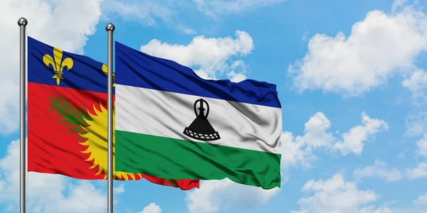 Bandera de Guadalupe y Lesotho ondeando en el viento contra el cielo azul nublado blanco juntos. Concepto diplomático, relaciones internacionales . — Foto de Stock