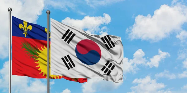 Guadeloupe en Zuid-Korea vlag zwaaien in de wind tegen witte bewolkte blauwe hemel samen. Diplomatie concept, internationale betrekkingen. — Stockfoto