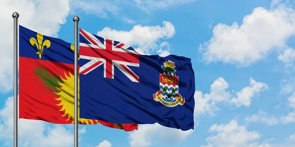 Bandera de Guadalupe y las Islas Caimán ondeando en el viento contra el cielo azul nublado blanco juntos. Concepto diplomático, relaciones internacionales . — Foto de Stock