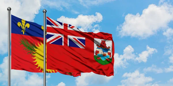 Guadalupe y la bandera de las Bermudas ondeando en el viento contra el cielo azul nublado blanco juntos. Concepto diplomático, relaciones internacionales . — Foto de Stock