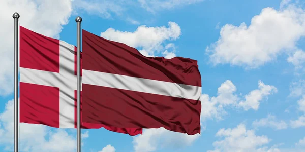 Drapeau du Danemark et de la Lettonie agitant dans le vent contre ciel bleu nuageux blanc ensemble. Concept de diplomatie, relations internationales . — Photo