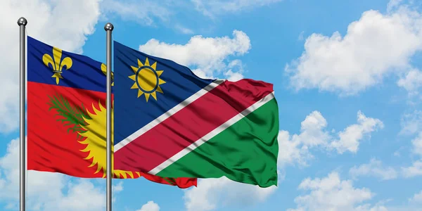 Guadalupe y la bandera de Namibia ondeando en el viento contra el cielo azul nublado blanco juntos. Concepto diplomático, relaciones internacionales . — Foto de Stock