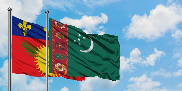 Bandera de Guadalupe y Turkmenistán ondeando en el viento contra el cielo azul nublado blanco juntos. Concepto diplomático, relaciones internacionales . — Foto de Stock