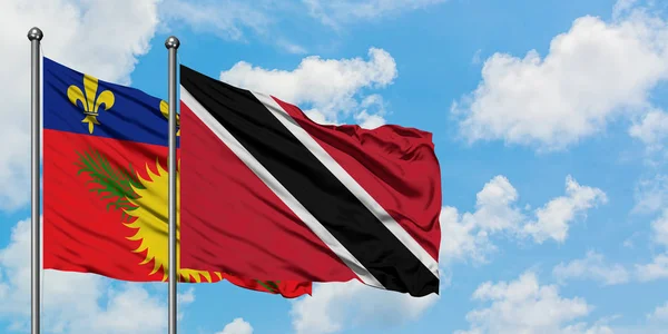 Guadeloupe ve Trinidad ve Tobago bayrağı birlikte beyaz bulutlu mavi gökyüzüne karşı rüzgarda sallayarak. Diplomasi kavramı, uluslararası ilişkiler. — Stok fotoğraf