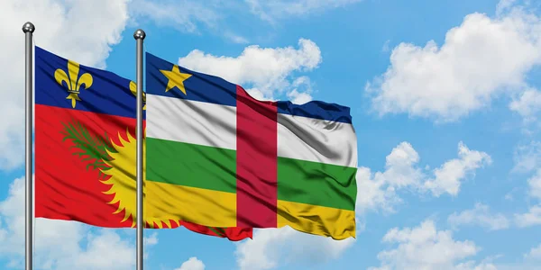 Guadalupe y la República Centroafricana ondean en el viento contra el cielo azul nublado blanco juntos. Concepto diplomático, relaciones internacionales . — Foto de Stock