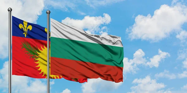 Guadalupe y la bandera de Bulgaria ondeando en el viento contra el cielo azul nublado blanco juntos. Concepto diplomático, relaciones internacionales . — Foto de Stock