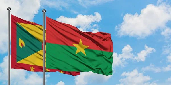 Bandera de Granada y Burkina Faso ondeando en el viento contra el cielo azul nublado blanco juntos. Concepto diplomático, relaciones internacionales . — Foto de Stock