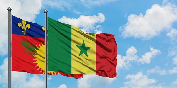 Guadalupe y Senegal ondean en el viento contra el cielo azul nublado blanco juntos. Concepto diplomático, relaciones internacionales . — Foto de Stock