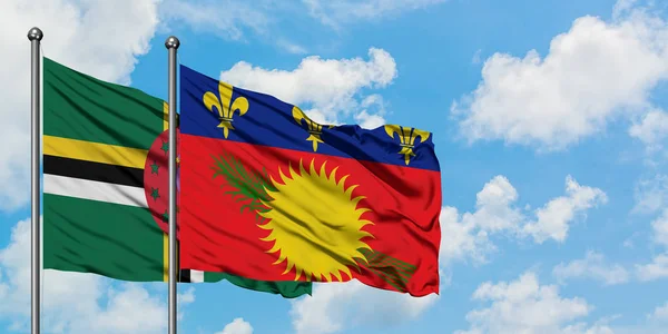 Bandera de Dominica y Guadalupe ondeando en el viento contra el cielo azul nublado blanco juntos. Concepto diplomático, relaciones internacionales . — Foto de Stock