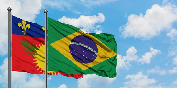Guadalupe y la bandera de Brasil ondeando en el viento contra el cielo azul nublado blanco juntos. Concepto diplomático, relaciones internacionales . — Foto de Stock