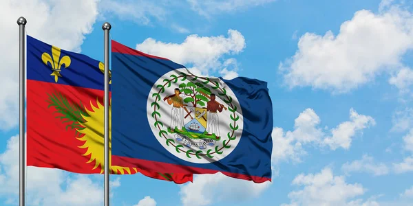 Guadalupe y la bandera de Belice ondeando en el viento contra el cielo azul nublado blanco juntos. Concepto diplomático, relaciones internacionales . — Foto de Stock