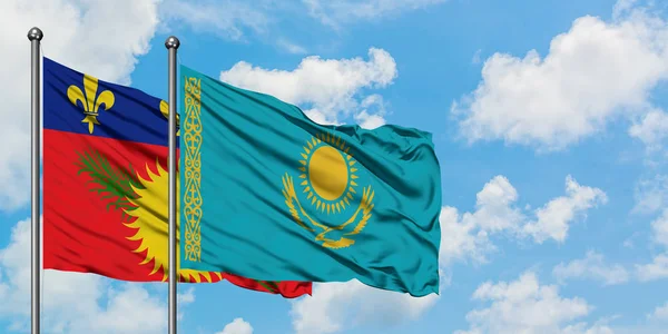 Guadalupe y la bandera de Kazajstán ondeando en el viento contra el cielo azul nublado blanco juntos. Concepto diplomático, relaciones internacionales . — Foto de Stock