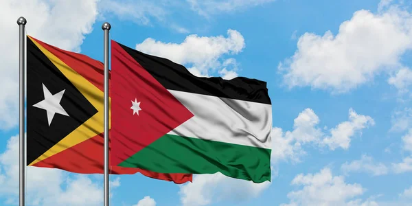 Timor Oriental y la bandera de Jordania ondeando en el viento contra el cielo azul nublado blanco juntos. Concepto diplomático, relaciones internacionales . — Foto de Stock