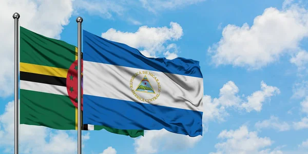 Dominica och Nicaragua flagga vifta i vinden mot vit grumlig blå himmel tillsammans. Diplomatisk koncept, internationella relationer. — Stockfoto