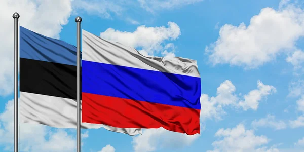 Estland und Russland wehen gemeinsam im Wind vor dem wolkenverhangenen blauen Himmel. Diplomatie-Konzept, internationale Beziehungen. — Stockfoto