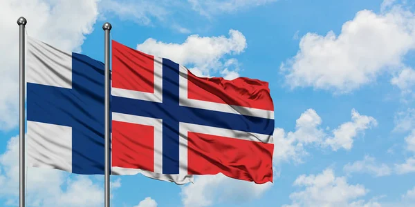 Bandera de Finlandia y Bouvet Islands ondeando en el viento contra el cielo azul nublado blanco juntos. Concepto diplomático, relaciones internacionales . — Foto de Stock