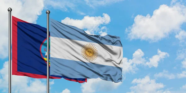 Guam e a bandeira da Argentina agitando no vento contra o céu azul nublado branco juntos. Conceito de diplomacia, relações internacionais . — Fotografia de Stock