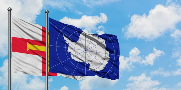 Vlajka Guernsey a Antarktidy mával ve větru proti bílé zatažené modré obloze dohromady. Diplomacie, mezinárodní vztahy. — Stock fotografie