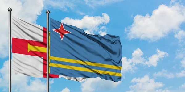 Guernsey y la bandera de Aruba ondeando en el viento contra el cielo azul nublado blanco juntos. Concepto diplomático, relaciones internacionales . — Foto de Stock
