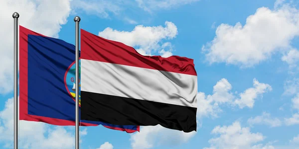 Guam e a bandeira do Iêmen agitando no vento contra o céu azul nublado branco juntos. Conceito de diplomacia, relações internacionais . — Fotografia de Stock