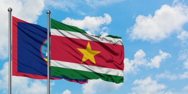 Guam ve Surinam bayrağı birlikte beyaz bulutlu mavi gökyüzüne karşı rüzgarda sallayarak. Diplomasi kavramı, uluslararası ilişkiler.