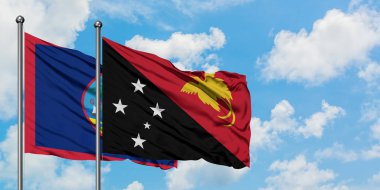 Guam ve Papua Yeni Gine bayrağı birlikte beyaz bulutlu mavi gökyüzüne karşı rüzgarda sallayarak. Diplomasi kavramı, uluslararası ilişkiler.