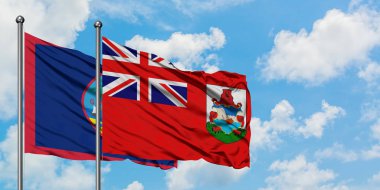 Guam ve Bermuda bayrağı birlikte beyaz bulutlu mavi gökyüzüne karşı rüzgarda sallayarak. Diplomasi kavramı, uluslararası ilişkiler.